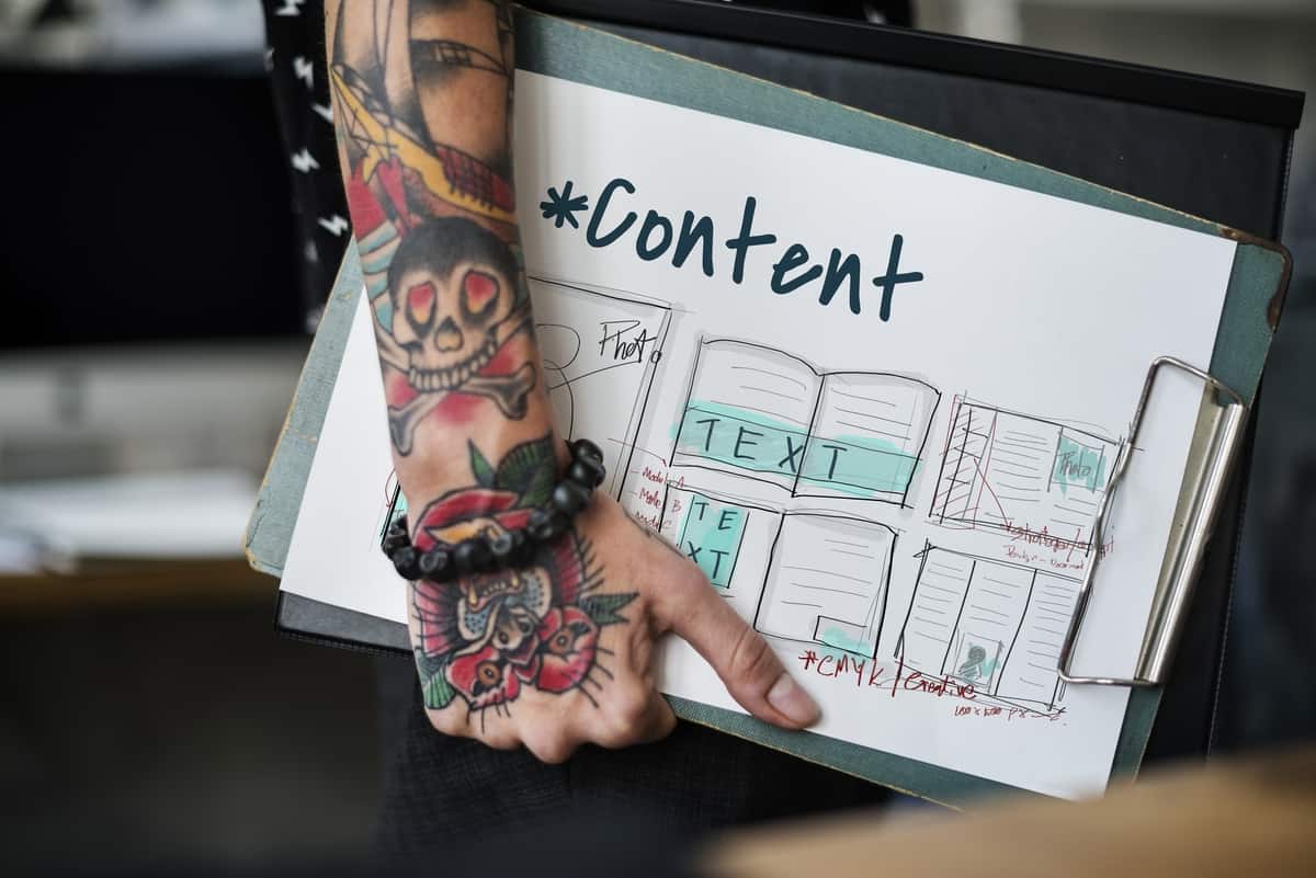 A tattooed ar holding a clipboard with a paper on the top that says 'content' with handdrawn design.
