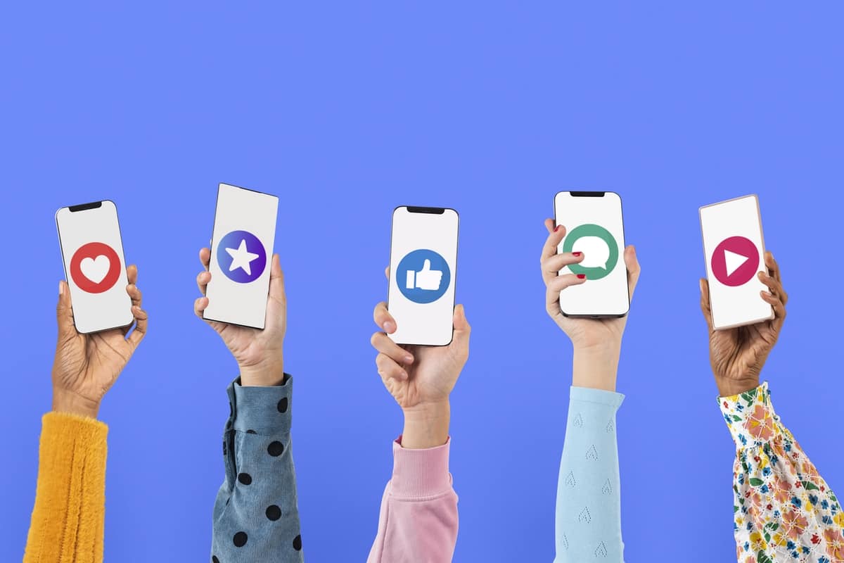 Hands holding smartphones with Facebook icons on the screens. There is a solid blue background.