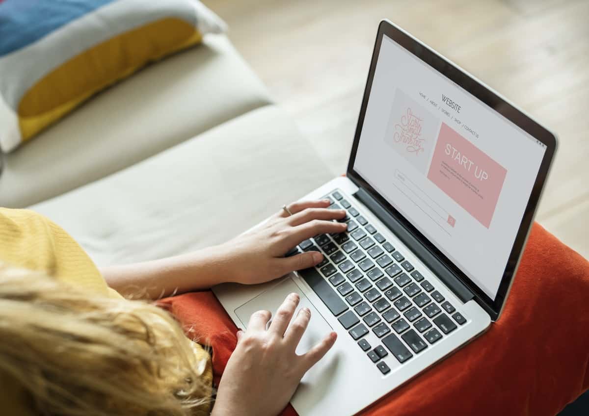 Woman with long blond hair sits with a laptop open to a landing page of a website. The screen has the words 'start up' in pink fancy lettering..